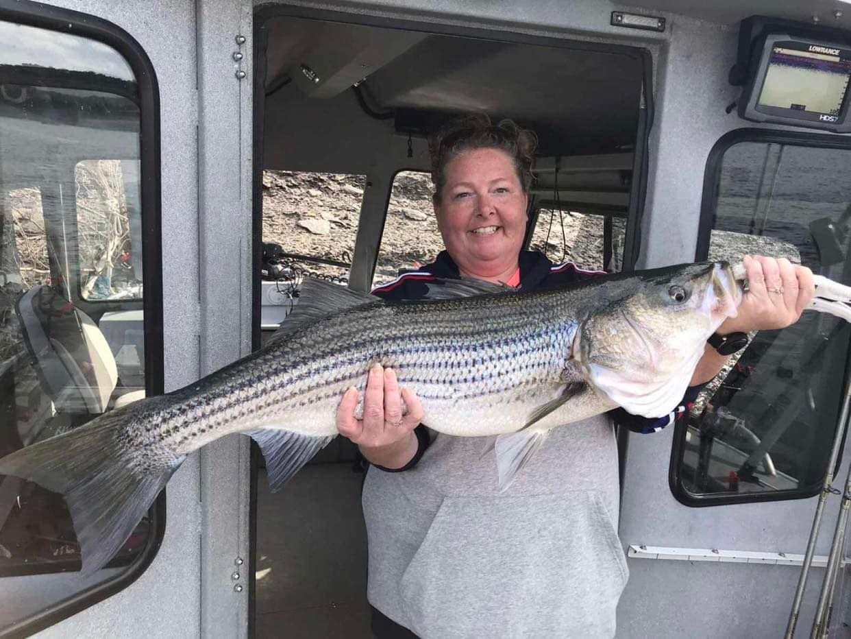 a smiling lady holding a larger striper
