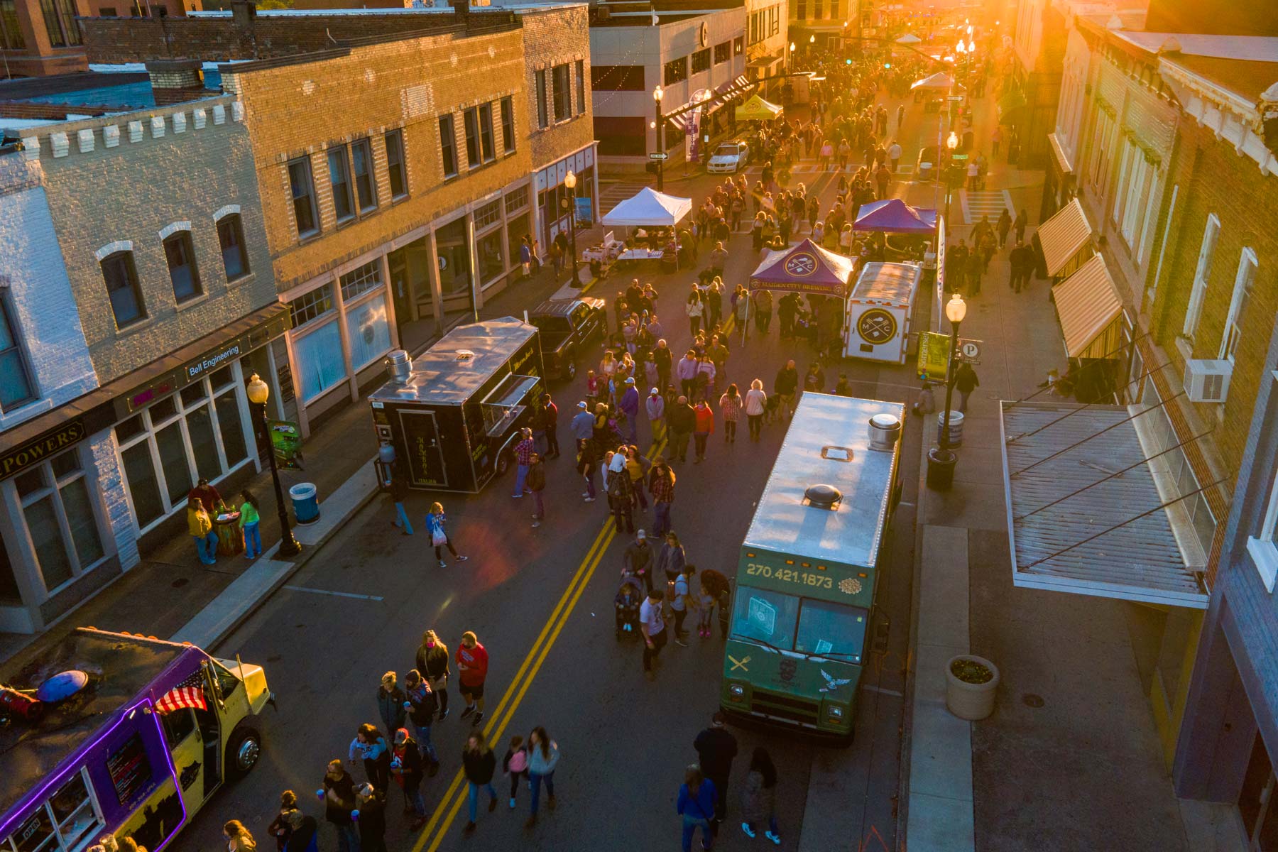Street view of people and food trucks at sunset.